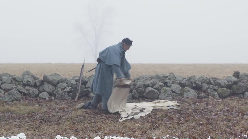 The man is laying a blanket on the ground