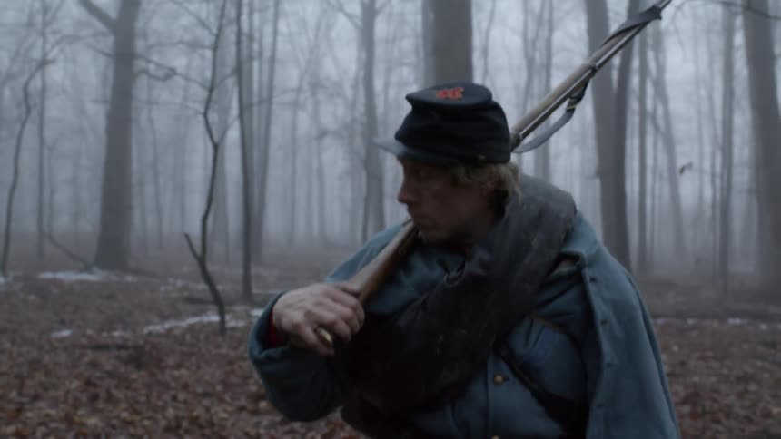 A soldiers carries a rifle in a foggy forest