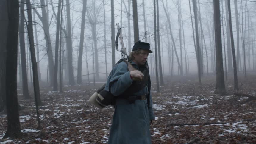 A soldier is carrying his rifle as he walks through a forest on a foggy morning