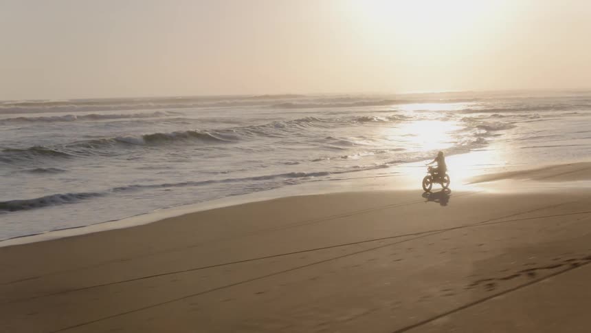 A motorcyclist rides on a beach at sunset