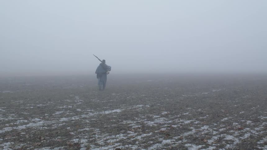 A soldier carries a rifle across a foggy field