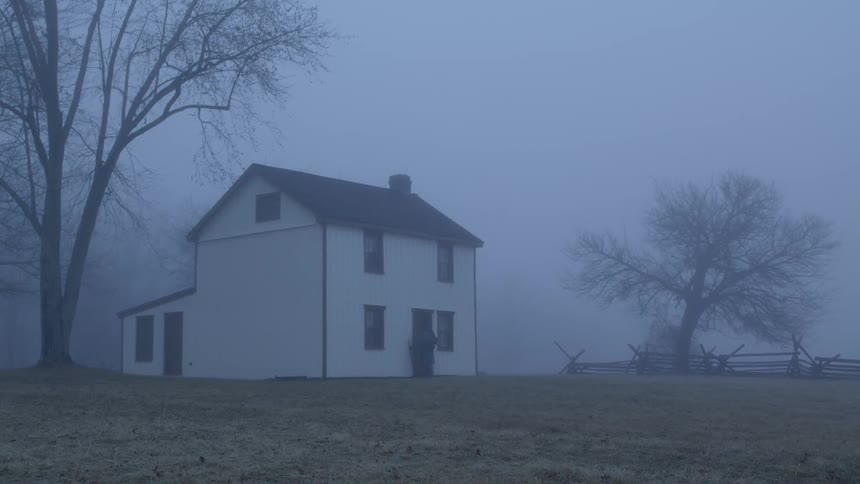 A person approaches a rural house in the fog