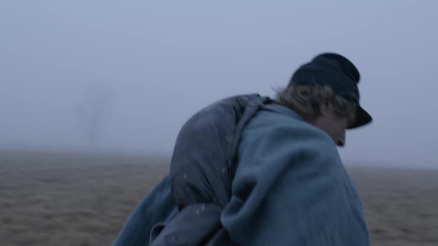 A soldier is putting his hat on and heading across a field on a foggy day