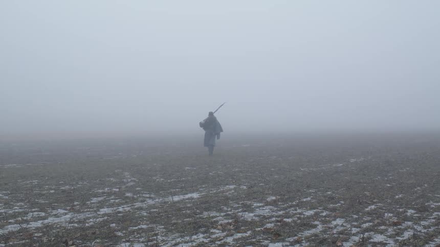 Soldier with rifle walks across snow covered field