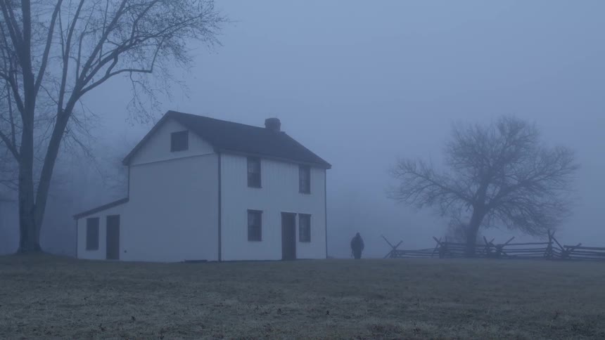 A person walks towards a house on a foggy day