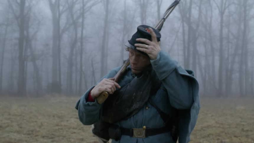 A soldier walks through a forest with a rifle