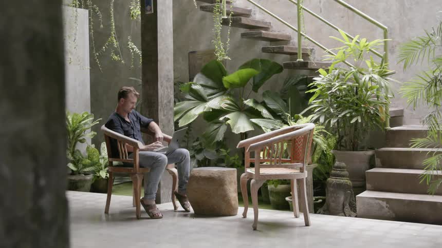 A man sits on a patio chair working on his laptop