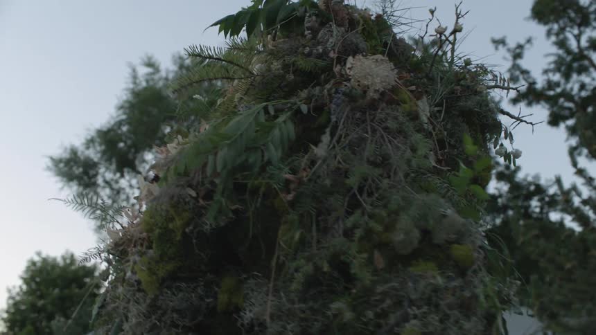 A person wearing a ghillie suit walks around outside