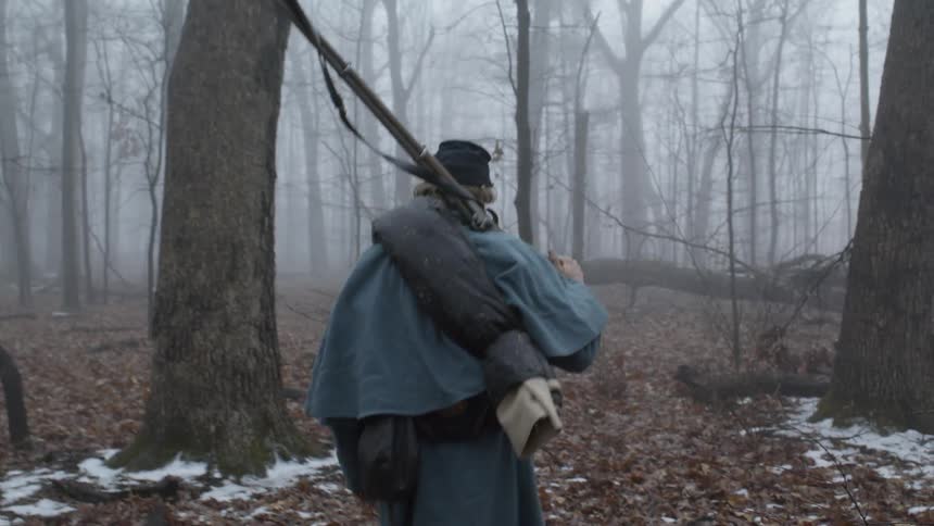 A soldier is carrying his rifle as he walks through a forest on a foggy morning