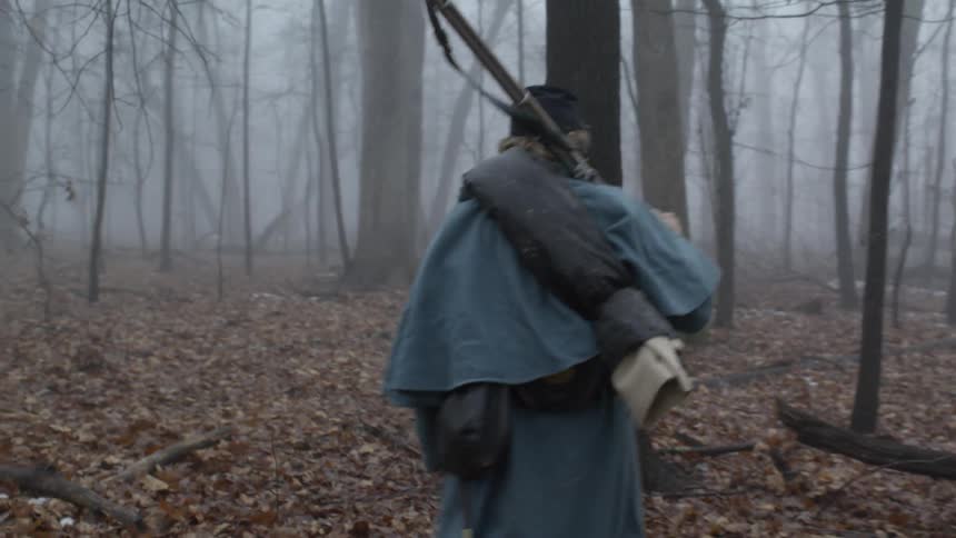 A soldier walks through the woods carrying a rifle on his shoulder