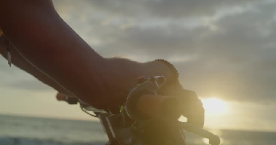 A man leans his crossed arms on motorcycle handlebars at sunset