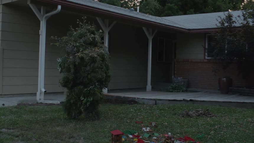 A person walks towards a house wearing a ghillie suit