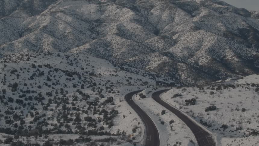 Vehicles travel on roads curving through snow and hills