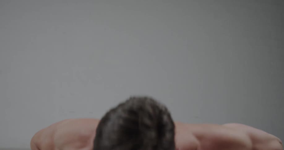 A man is slapping his chest as he does push ups inside in daylight