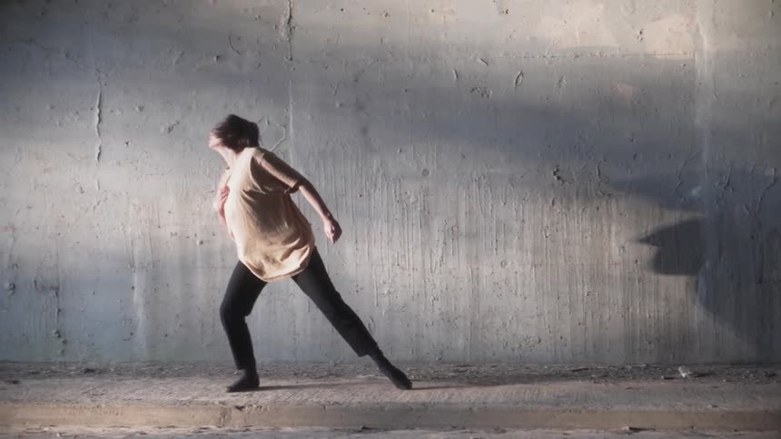 Woman dances outside next to a concrete wall