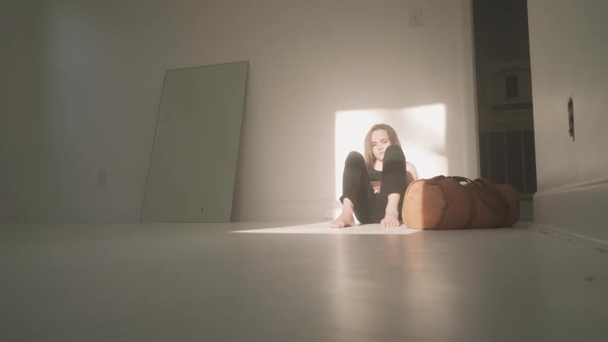 The woman is sitting against the wall in the room