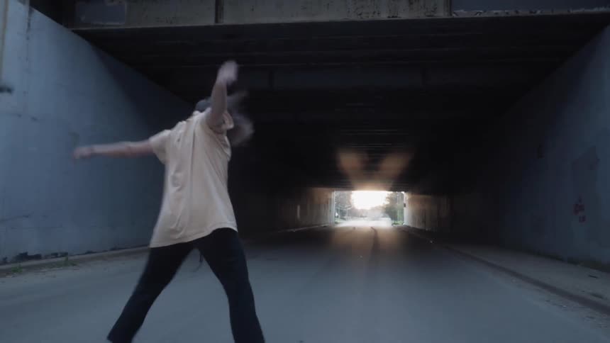 A woman dances and gestures under a bridge