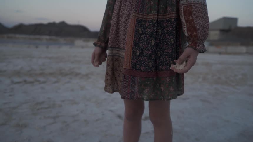 Girl crumbles sand in her hands outside at sunset