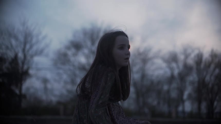 A  girl sits outside at sunset