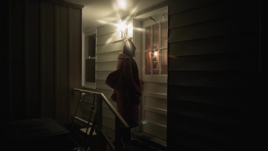 Woman walks out a house door at night