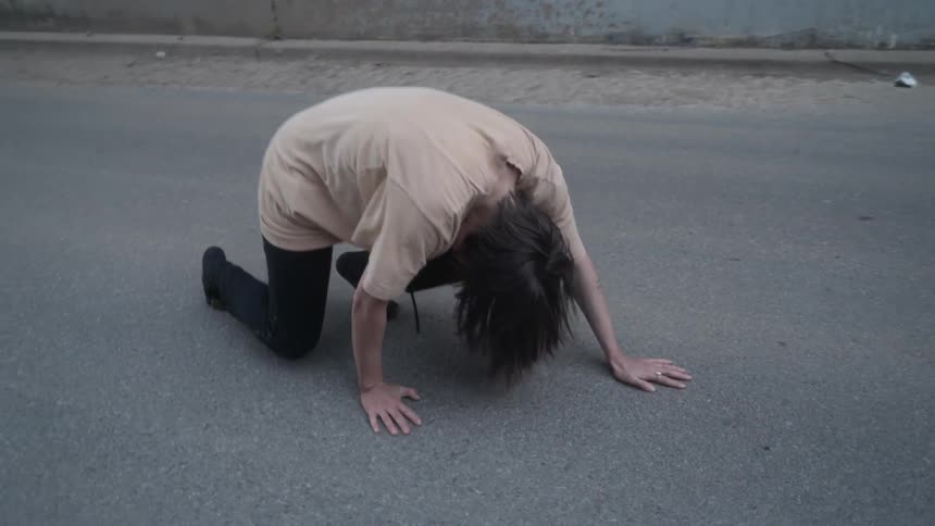 A woman dances on a road below an overpass