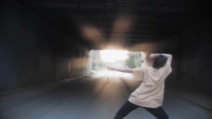 A woman is dancing inside a tunnel in an urban setting at dawn