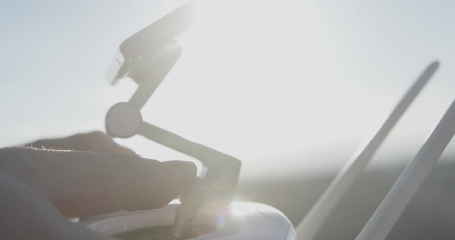 The sun shines and glares on the screen as a person controls a drone