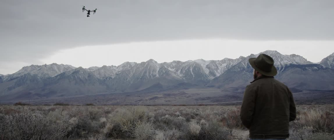 A drone rises and moves away over a desert landscape