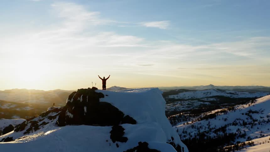 Man stands on top of a snowy mountain under a blue sky