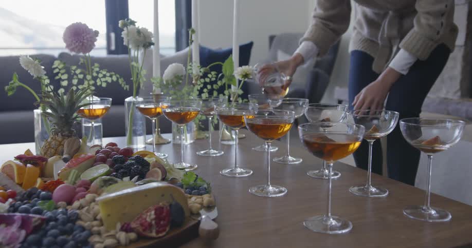 Person pours liquid into small cocktail glasses lined up on the table