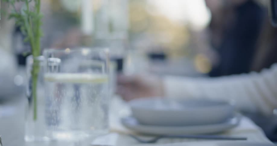 A person picks up a wine glass during an outdoor dinner party