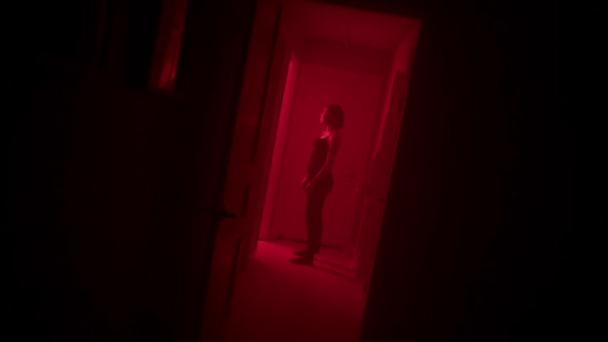 The woman is standing by the door down the dark hall