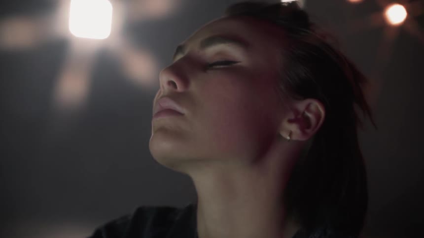 A woman stands under spotlights with her eyes closed