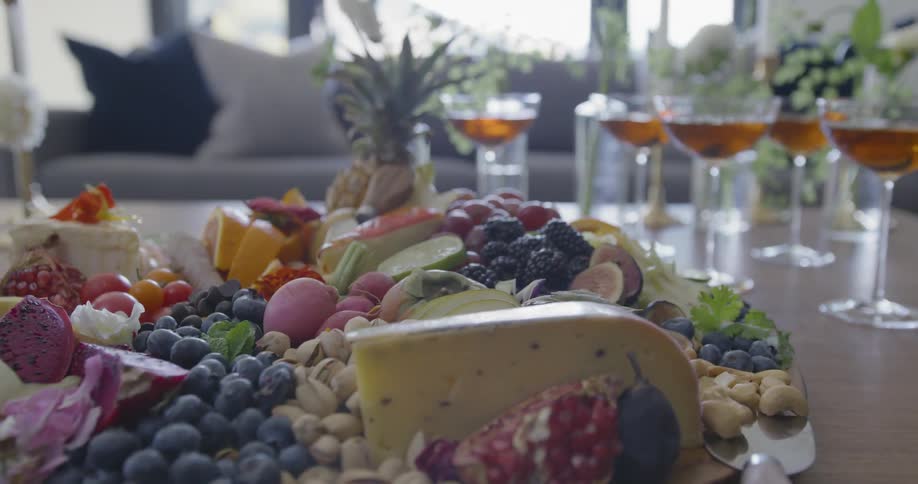 Pan around a plate of fruits and cheese next to wine glasses