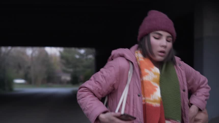 Girl walks under bridge and looks at cell phone