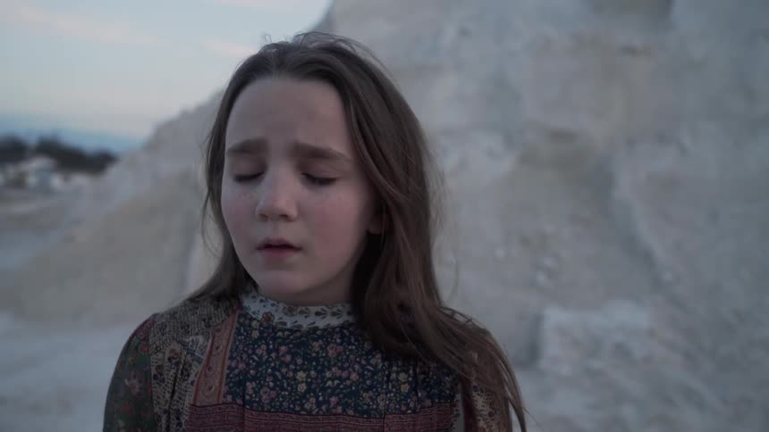 A sad girl stands outside with her eyes closed