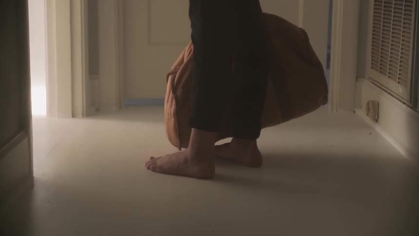 Barefoot person in hallway holding bag