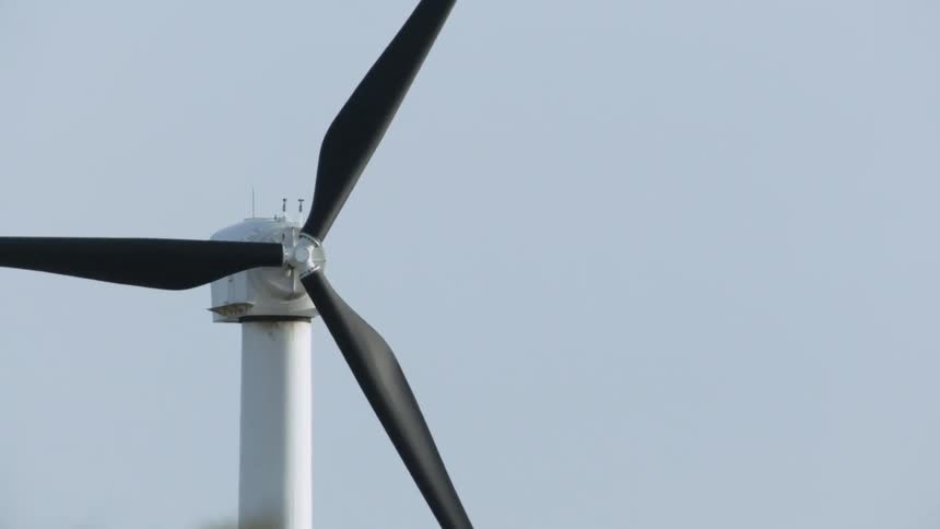The windmill has black blades that are turning slowly