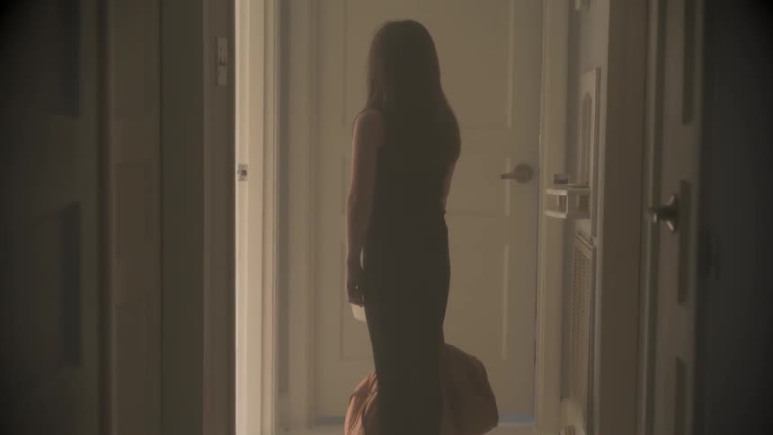 A woman holding a bag is standing in front of a door in a house in daylight