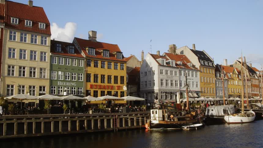 People walk along a pier where boats are docked in a coastal city