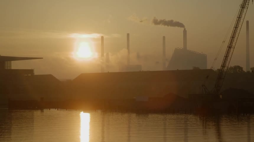 Smoke billows out of a smoke stack at sunset