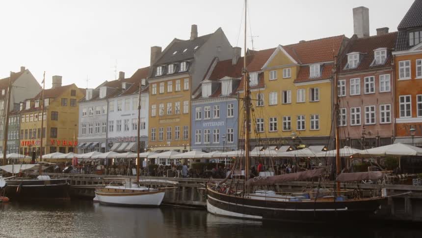 Boats sit docked in the water in front of a row of buildings