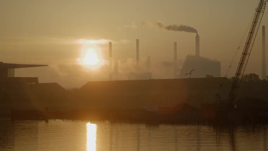 The sun sets behind a factory