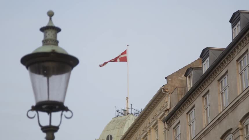 A red and white flag on top of a building waves in the wind