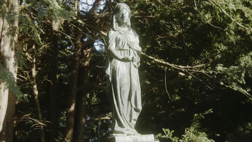 A statue of a woman sits by the trees