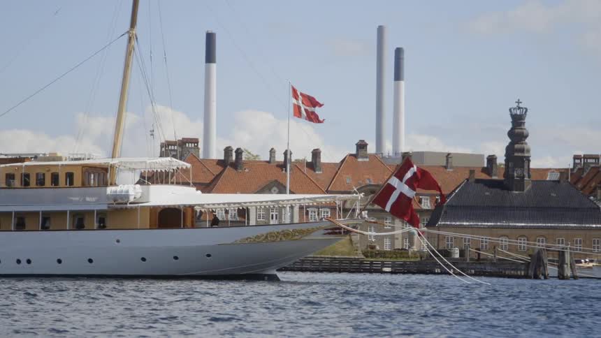 A boat and a building in a harbor are flying the flag of denmark during the day