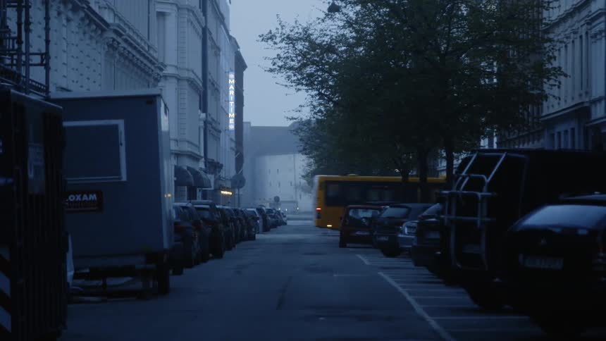 A bus travels past a road with cars parked on both sides