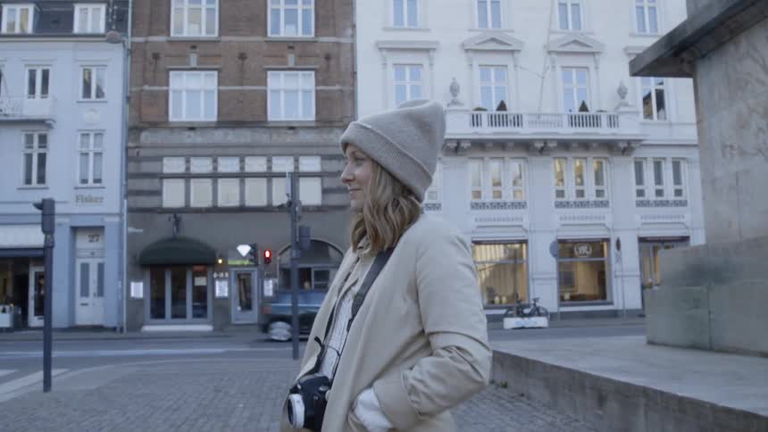 A woman is smiling as she stands outside in an old part of a city on a cold day