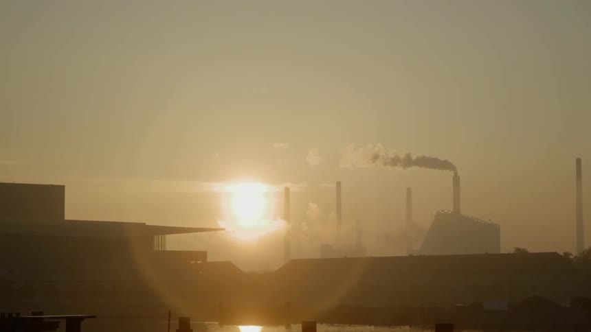 The sun sets behind a factory