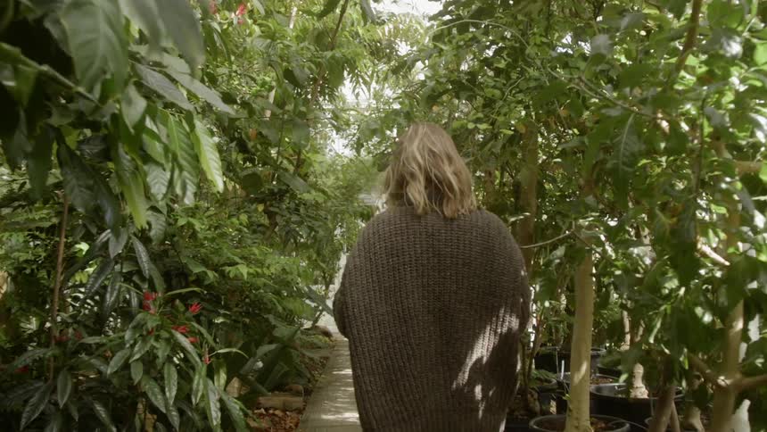 A woman walks by plants in a nursery